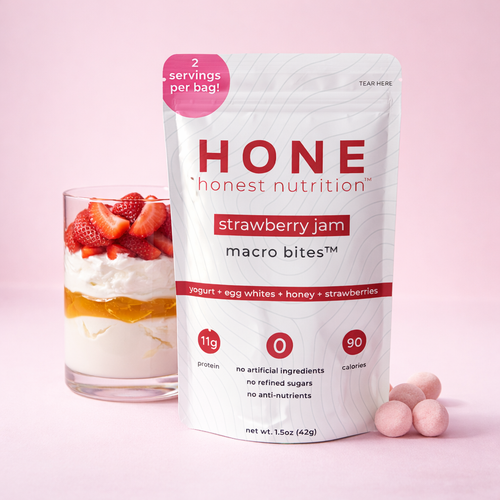 honest nutrition strawberry jam macro bites package with a glass of yogurt and strawberries on a pink background